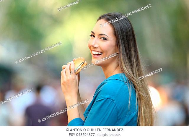 Happy woman eating a burger looking at camera in the street