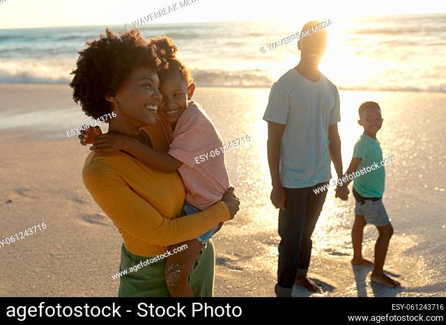 Happy african american mother carrying daughter while standing by father and son at beach