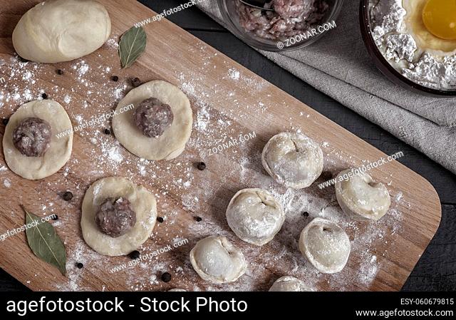 Cooking homemade dumplings, Russian dumplings with meat on a wooden table and ingredients for cooking. Rustic style. Top view with copy space