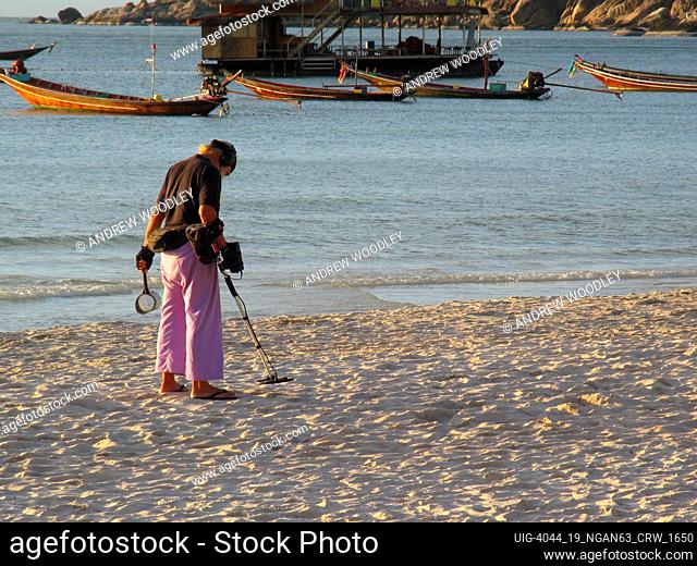 Prospector at dawn with metal detector on Sunset Beach Ko Pha Ngan island Thailand