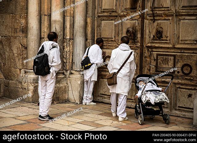 05 April 2020, Israel, Jerusalem: People pray outside the closed door of the Church of the Holy Sepulchre during the Catholic Palm Sunday