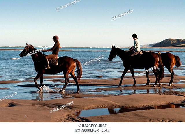 Two women riding horses on beach