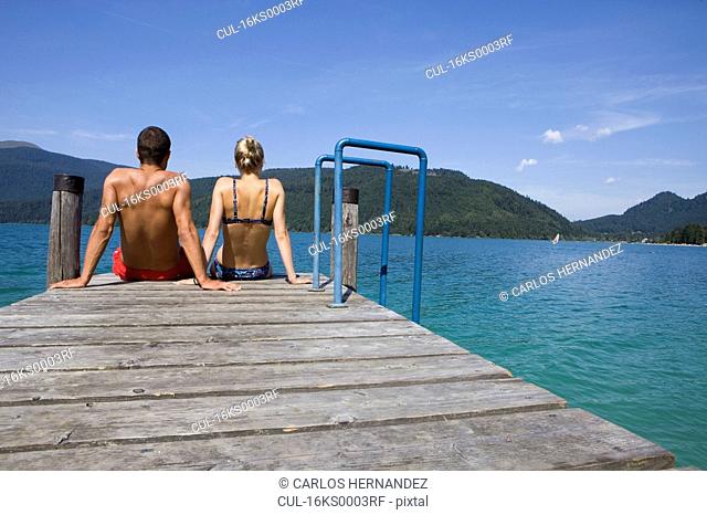 A couple sitting on a pier by a lake