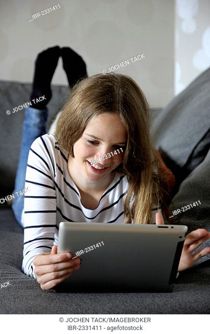 Girl lying on a sofa holding an iPad, tablet computer with wireless internet access