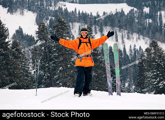 Man standing with arms outstretched by skis