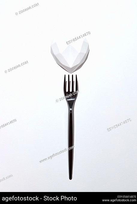 Creative holiday set from white plaster heart and plastic disposable black fork on a light grey background with copy space
