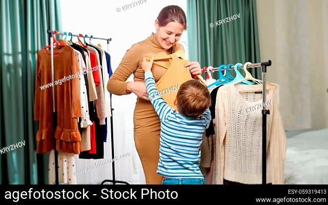 Young pregnant mother with little son choosing clothes to wear in wardrobe at bedroom