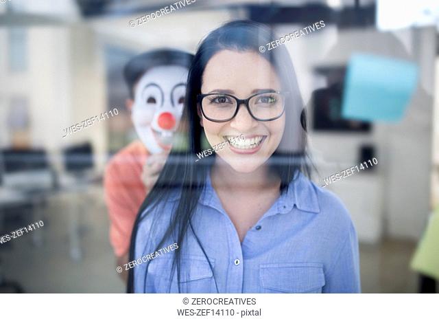 Employee smiling while someone with a clown mask is behind her