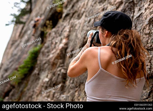 A low angle and rear view of a slim caucasian female sports and adventure photographer at work during a rock climbing competition. Copy space to left