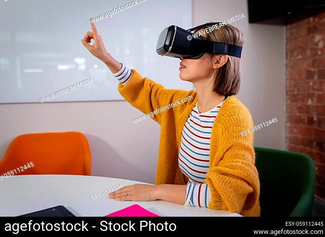 Asian businesswoman sitting at work wearing virtual reality set and playing
