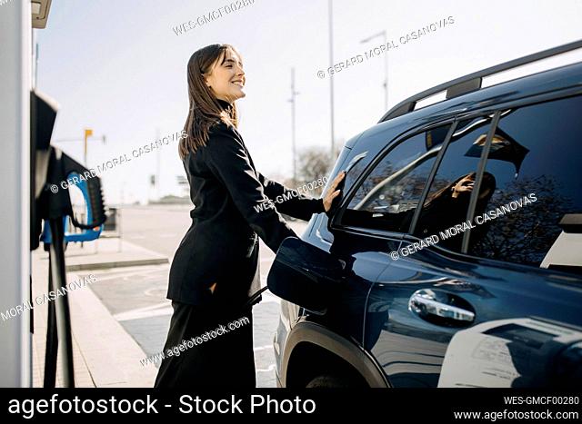 Smiling businesswoman charging electric car at charging station