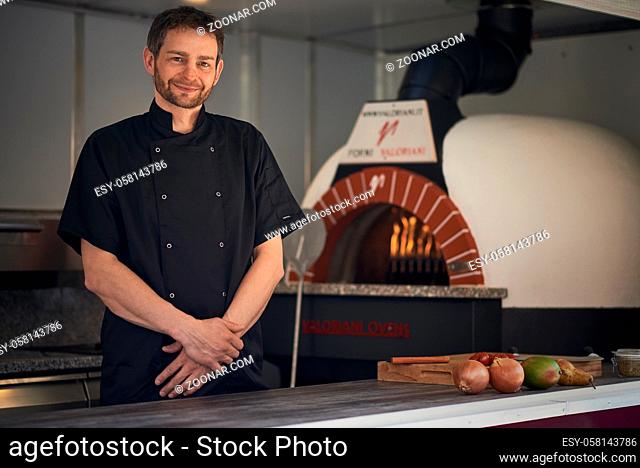 Smiling chef baking or flame grilling an Italian pizza in a modern wood oven at a pizzeria