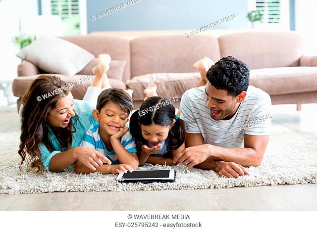 Parents and children lying on rug and using digital tablet in living room