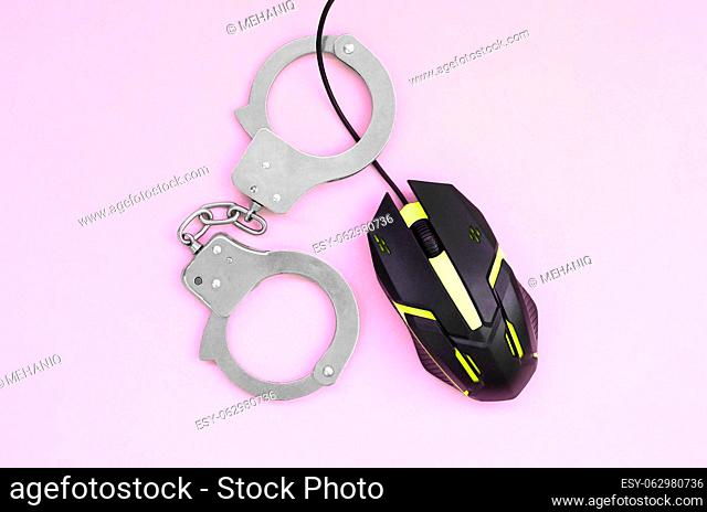 Computer mouse in a yellow color is chained in handcuffs on the background of pink color. The concept of combating computer crime, hackers and piracy