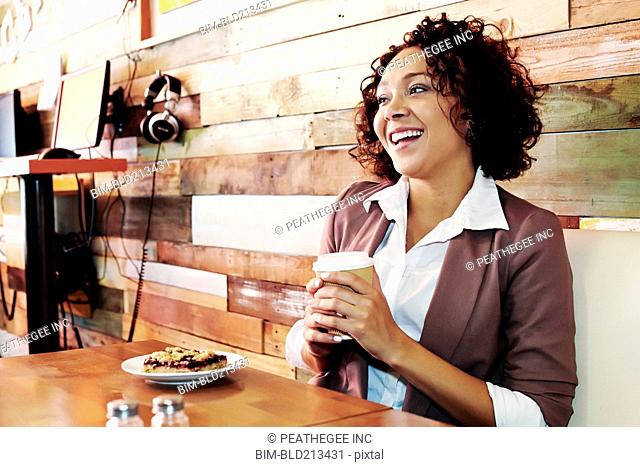 Mixed race businesswoman having coffee and pastry in cafe