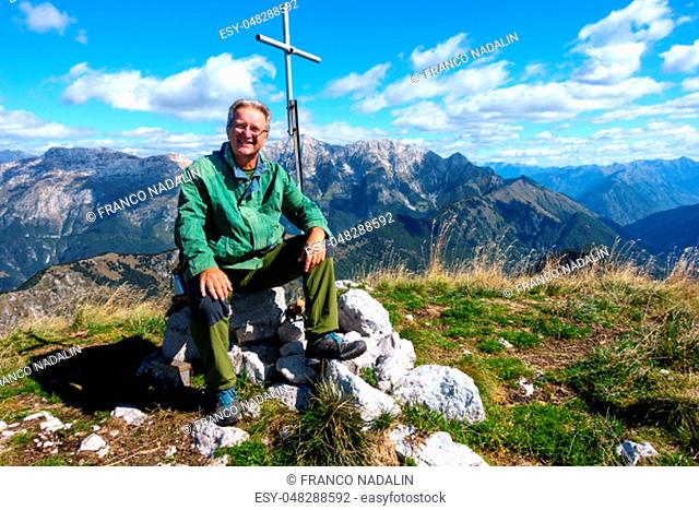 Mature hiker sitting on peak and smiling and looking on camera