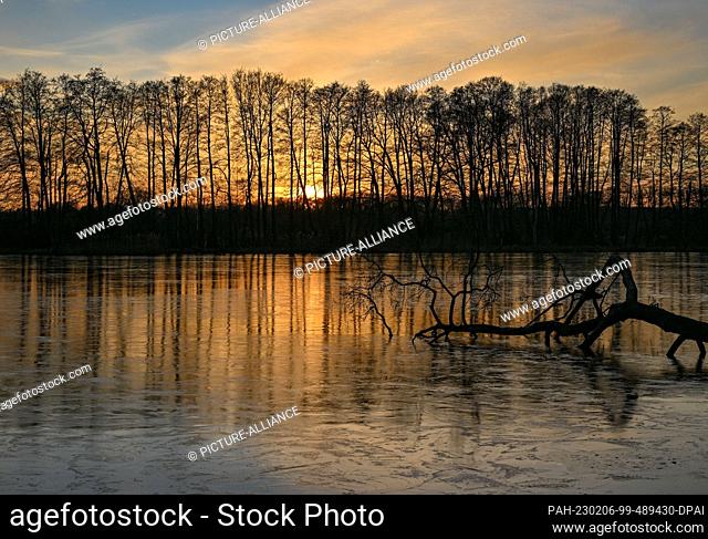05 February 2023, Brandenburg, Lietzen: The sunset shines colorfully over a small lake in eastern Brandenburg, reflected in the ice on the water