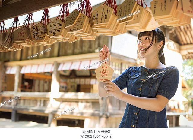 Young woman wearing blue dress looking at wooden fortune telling plaques at Shinto Sakurai Shrine, Fukuoka, Japan