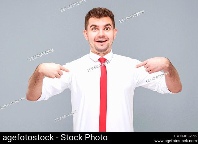 Portrait of young shocked handsome man in white shirt and tie standing with shocked face, pointing himself and looking at camera with shocked face