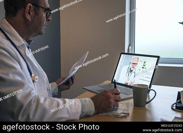 Doctor discussing medical report with colleague on video call at office
