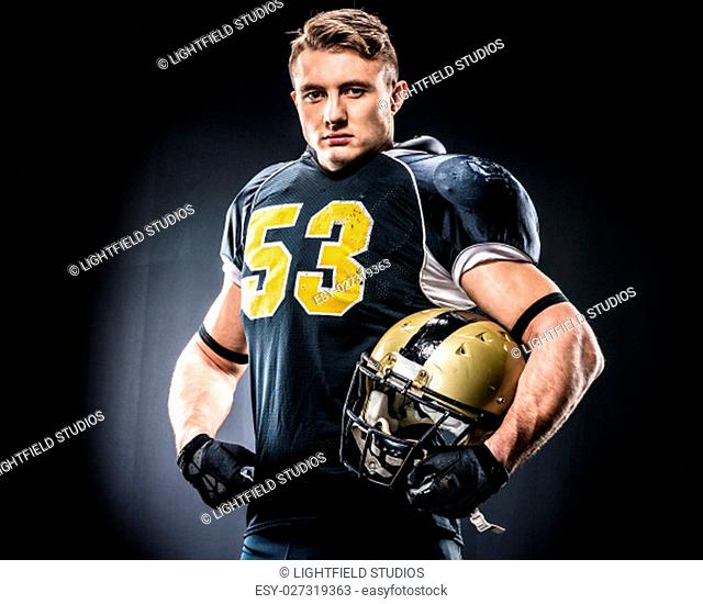 American football player holding helmet and looking at camera on black