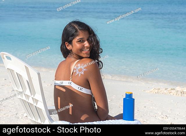 Tanned body hispanic girl painted Sunny on shoulder with sun protection cream