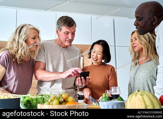 Senior man looking for recipes on smart phone while gathered with friends