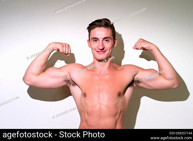 Studio shot of young handsome muscular man with brown hair shirtless against white background