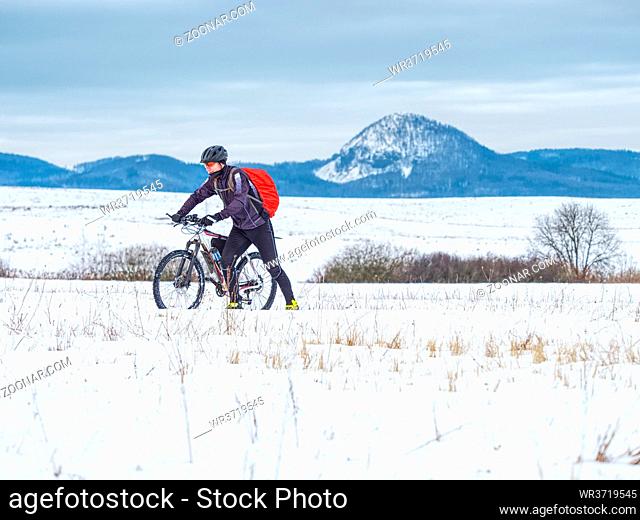 Mountain biker in snowy landscape. Sportsman properly equiped for winter cycling is ridding in heavy terrain. Sunny winter weather and snow