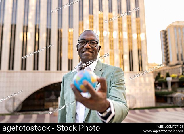 Happy mature businessman with globe figurine standing in front of building