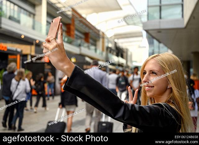 Close up portrait of an attractive young urban girl while taking selfie with her cell phone in the busy and crowded business district of London, United Kingdom