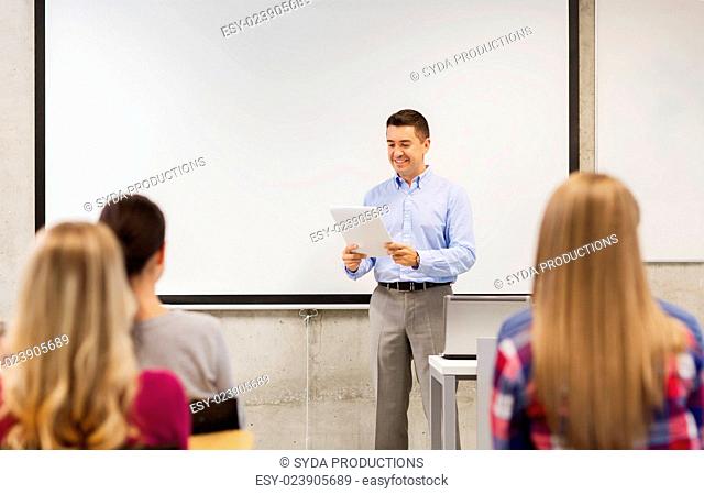 education, high school, technology and people concept - smiling teacher with notepad, laptop computer standing in front of students and showing something on...