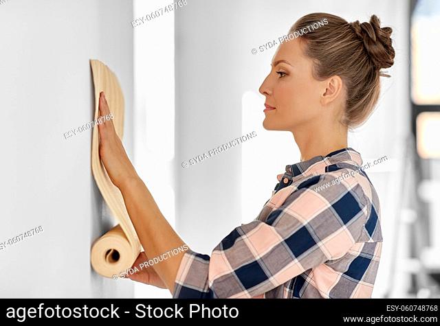 woman applying wallpaper to wall at home
