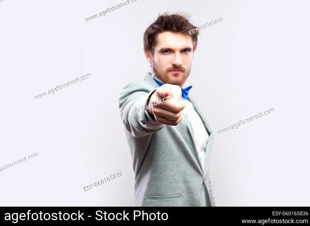 Portrait of serious handsome bearded man in casual grey suit and blue bow tie standing and looking and blaming at camera