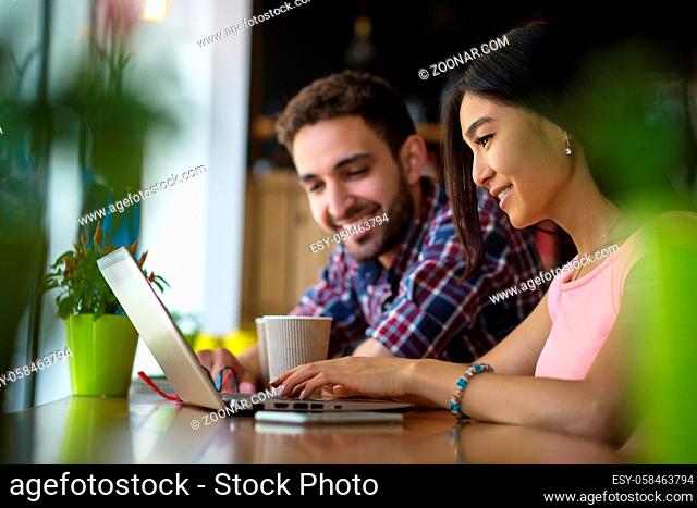 Picture of happy business or freelance man and woman working on laptop computer in restaurant or cafe. Asian lady showing ner business project to his partner or...