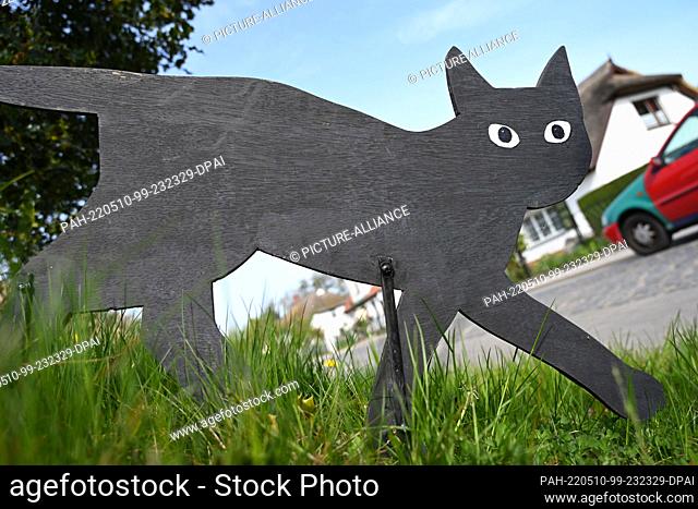 10 May 2022, Mecklenburg-Western Pomerania, Born: A wooden cat stands in sunny weather as a car scare in a traffic-calmed area in a village street in the...