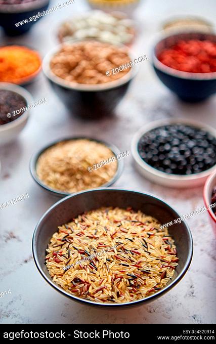 Raw wold rice seeds in ceramic bowl. Composition of superfoods in background. Placed on white rusty table. Selective focus