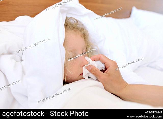Mother wiping nose of daughter lying on bed at home