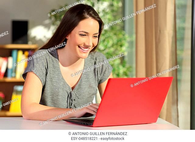 Casual single beautiful and happy housewife writing an e mail on line in a red laptop sitting in a table at home