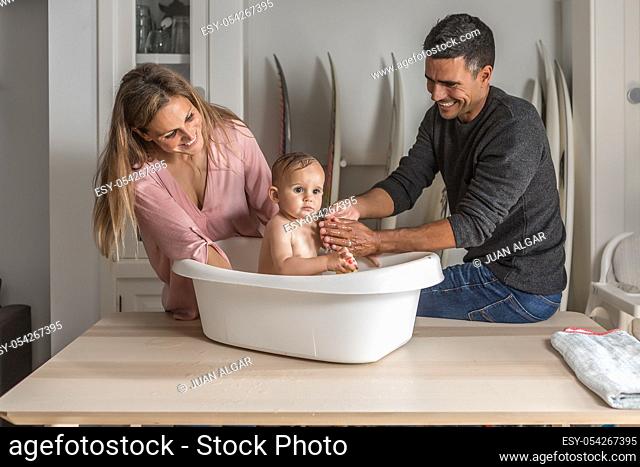 Dad and mon have fun bathing the baby in the bathtub