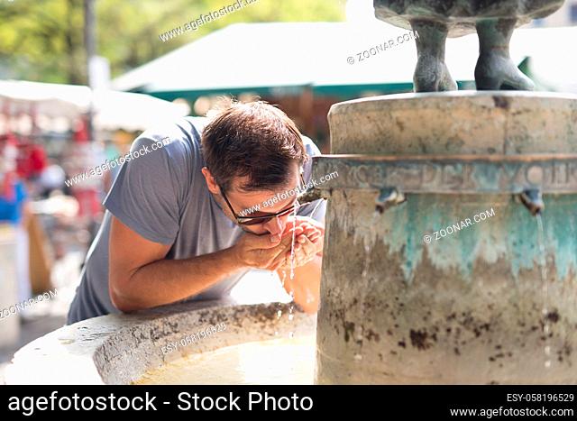 Thirsty young casual cucasian man drinking water from public city fountain on a hot summer day