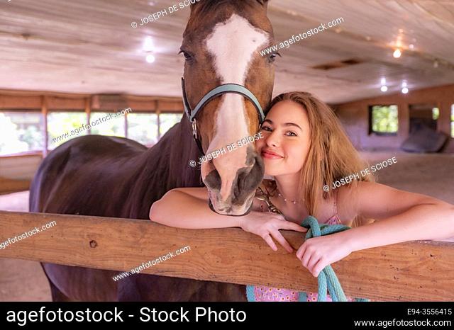 A 14 year old brunette girl and her horse in a stable
