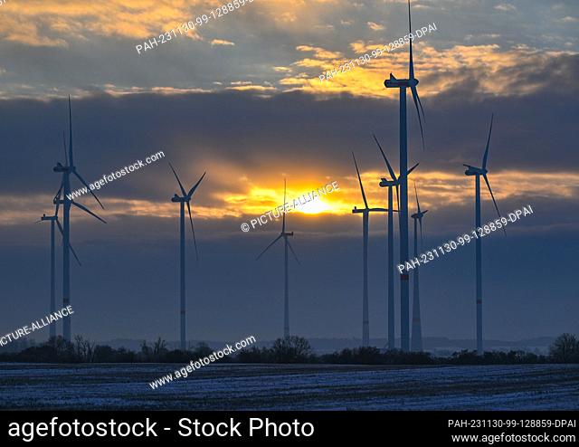 30 November 2023, Brandenburg, Petersdorf: The sun rises through dense clouds early in the morning over a wind farm in the Oder-Spree district in the east of...