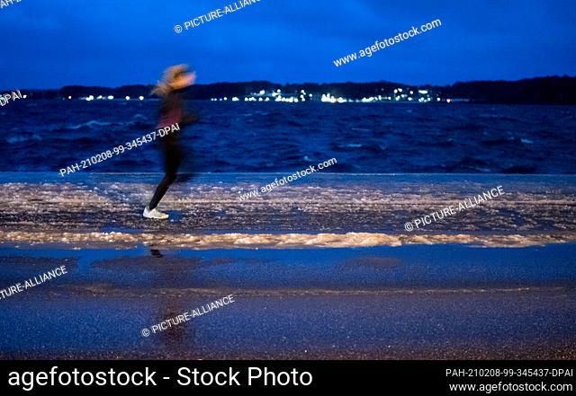 08 February 2021, Schleswig-Holstein, Kiel: An early morning jogger runs near the shore of the Baltic Sea on a road on which a layer of ice has formed after...