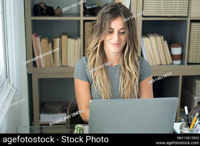 Modern millennial young woman work on computer at the desk in home office alternative business workstation. Female smile and watch pc display