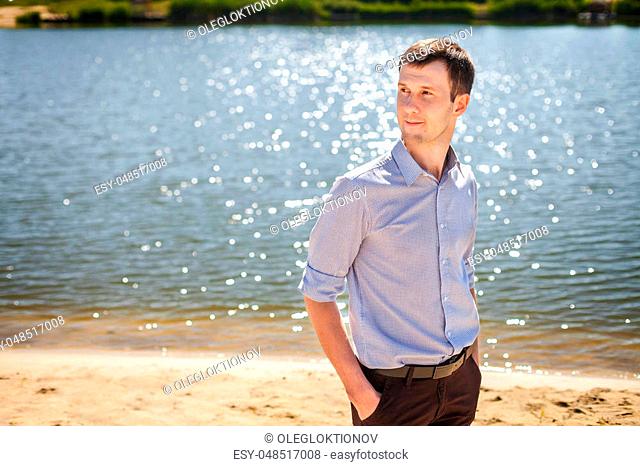 Young handsome man in blue shirt in pattern resting near lake, walking on coast