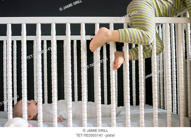 Girl (2-3) climbing on crib and brother (6-11 months) lying inside