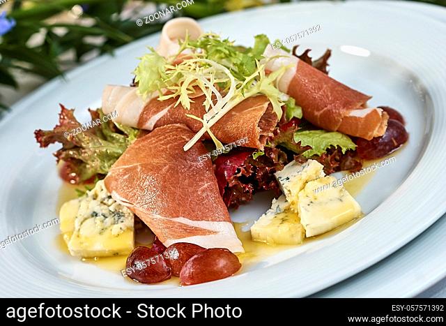 meat salad with ham cheese lettuce Dorblu grapes and olive oil served on a plate on a table with flowers