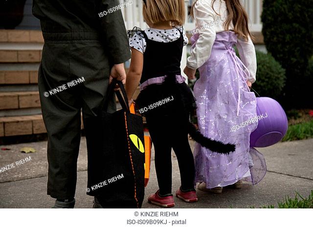 Boy and sisters trick or treating waiting at porch stairway