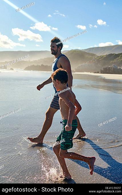 Father and son wading in sunny summer ocean surf